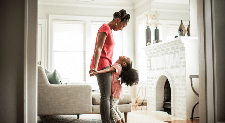 Woman and daughter holding hands and smiling in living room