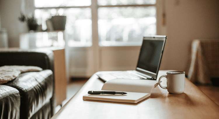 Notebook with a pen, coffee mug and a laptop on a coffee table